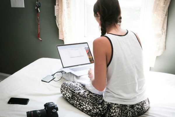 woman in white tank top sitting on bed in front of laptop computer